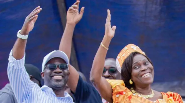 Simone Gbagbo, vêtue d'une tenue orange, se tient à droite de Charles Blé Goudé, qui porte une chemise rayée bleue et blanche et des lunettes.