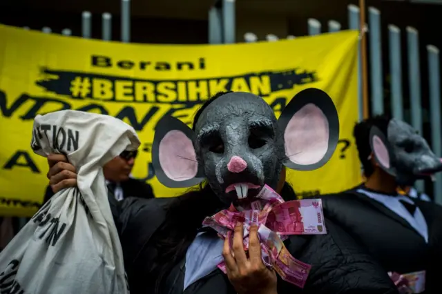 Seorang aktivis antikorupsi sedang melakukan aksi seni dengan kostum tikus meraup uang.