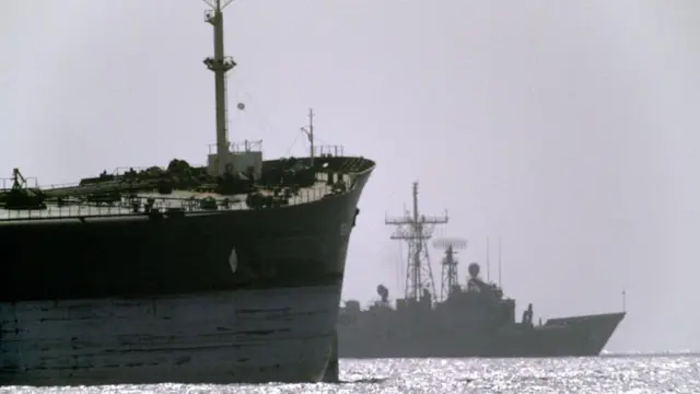 Američki ratni brod u pozadini putuje pored teretnog broda tokom operacije 'Iskrena namera' u Ormuskom moreuzu.