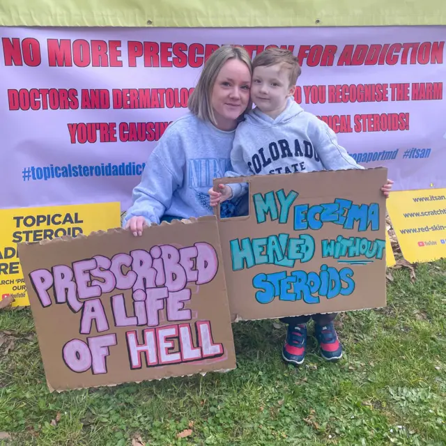베서니 노먼과 그의 아들이 스테로이드 사용에 반대하는 시위에서 피켓을 들고 있다.