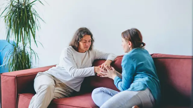 Dos mujeres hablan sentadas en su sofá mientras se agarran de las manos