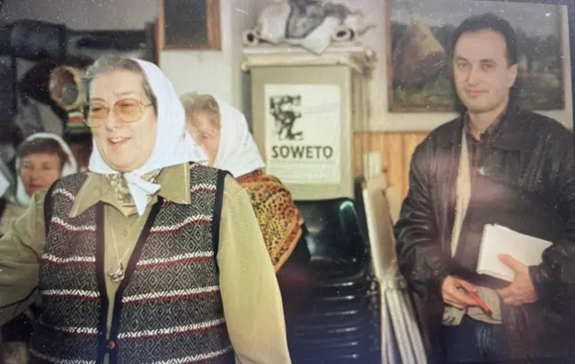 Uma mulher usando óculos e sorrindo. Ao lado dela está Nilson Mariano