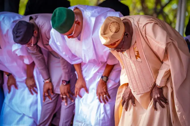 President Bola TInubu wear light brown cloth for di far right, near Vice President Kashim Shettima wey wear hite cloth and green cap.