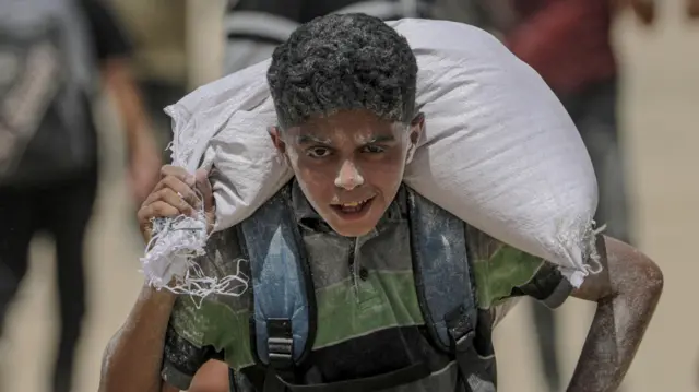 Palestinski dečak nosi kesu brašna blizu punkta za podelu hrane u Zikimu, na severu Gaze, 8. avgusta 2025. godine.