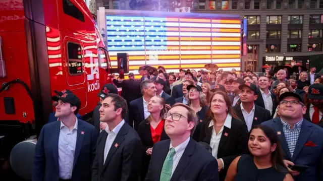 幾位身穿西裝的人站在時報廣場，站在一輛印有「Kodiak AI」字樣的紅色卡車旁，抬頭望向鏡頭外的上方。