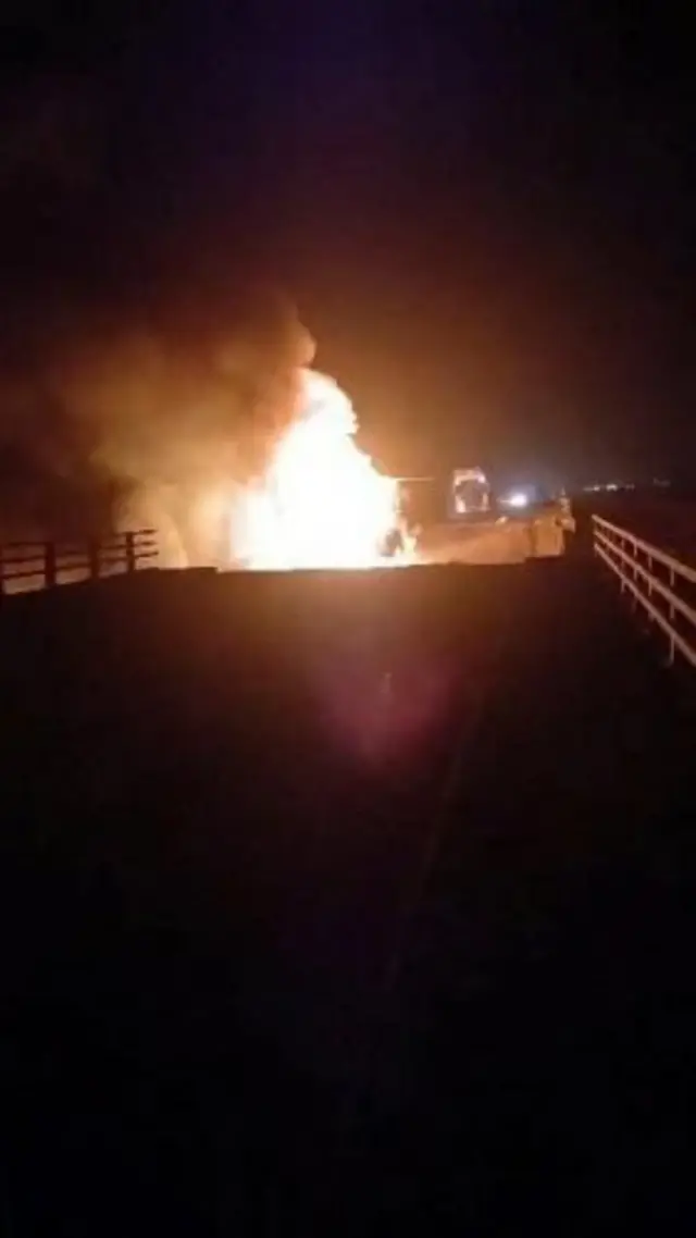 他は暗い夜の屋外で、左右に欄干が見える橋の中央から炎が上がっている