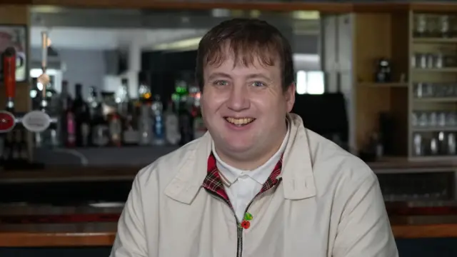Macaulay Robinson sidon for di clubhouse for Kirkley and Pakefield Football Club for Lowestoft in front of di old wooden style bar. 