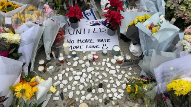 Ofrendas florales y un mensaje que lee: " Estamos unidos. No más odio. Más amor"