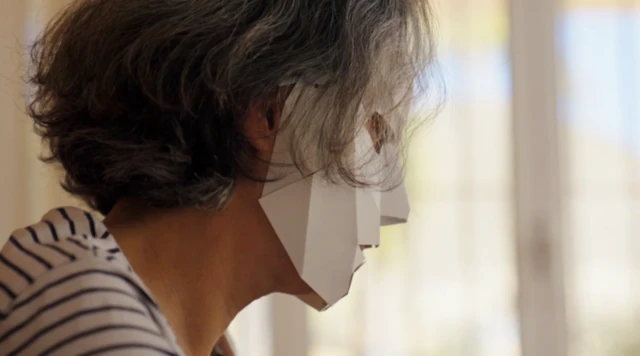 종이 마스크를 쓰고 책상 앞에 앉아 있는 마리아의 모습