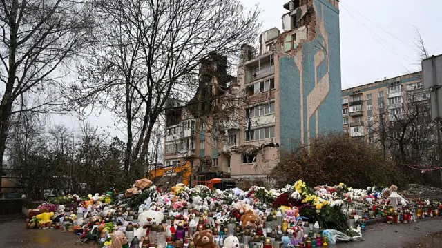 На фотографії імпровізований меморіал з іграшок, квітів і лампадок біля сильно пошкодженого житлового будинку в Тернополі 