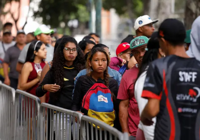 Pessoasfrutinha caça níquelfila; mulher carrega mochila com as cores da venezuela