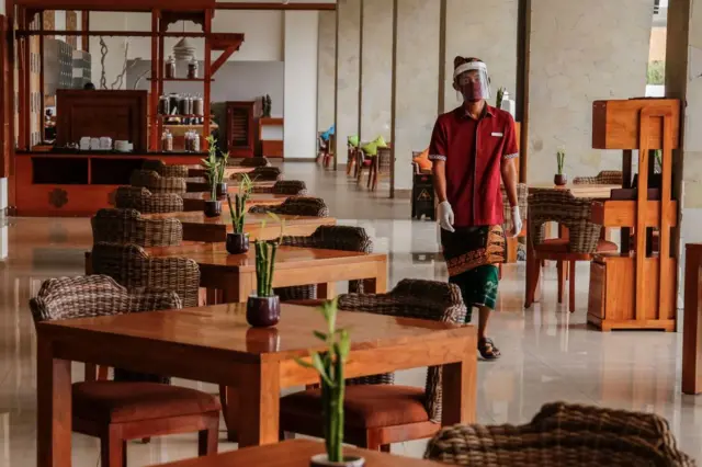 Staf restoran hotel mengenakan masker wajah, sarung tangan, dan pelindung wajah sebagai protokol kesehatan saat pandemi virus corona (Covid-19), berjalan di tengah restoran di Hotel Inaya Putri Bali di Nusa Dua, Bali, Indonesia pada 5 Juni 2020. 