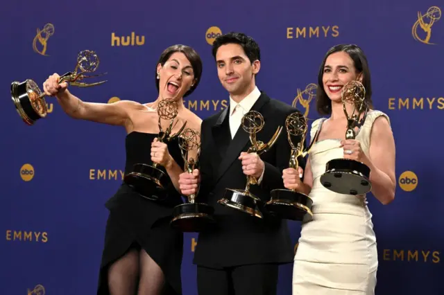 "Hacks" ile En İyi Komedi Dizisi Ödülü ve Komedi Dizisi Dalında En İyi Senaryo Ödülü'nü kazanan ABD'li yazar Jen Statsky, ABD'li aktör Paul W. Downs ve ABD'li yönetmen ve yazar Lucia Aniello.