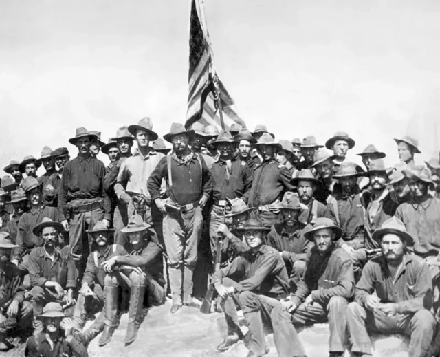 عکس سیاه و سفید، رئیس جمهور آینده، روزولت (وسط) را به همراه سربازان آمریکایی در تپه سن خوان در کوبا در طول جنگ اسپانیا و آمریکا نشان می‌دهد