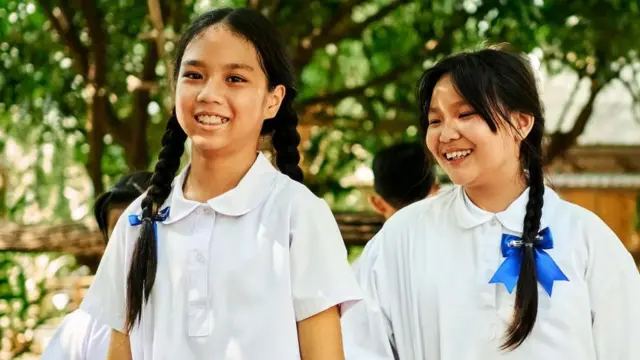Hai nữ sinh trẻ mặc áo trắng, tóc dài buộc hai bên.