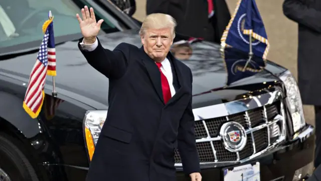 Donald Trump saludando con la mano derecha a la multitud reodeado de su equipo de seguridad