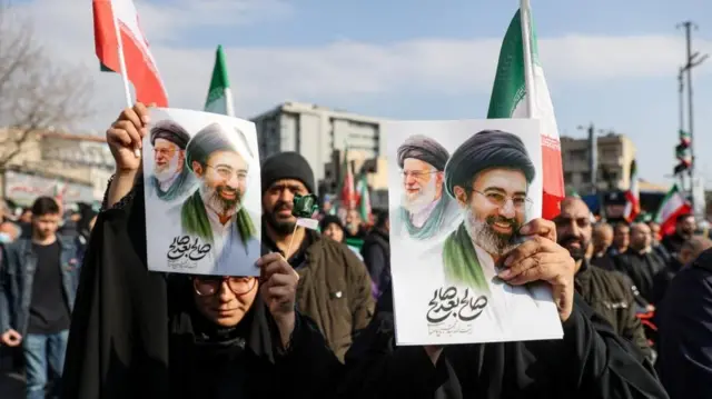 Apoiadores mostrando cartazes com Mojtaba Khamenei ao lado do seu pai, o aiatolá Ali Khamenei, em manifestações realizadas em Teerã