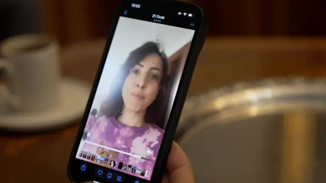 Müge Karataşlı yangın gecesi çektiği videoyu BBC röportajı için telefonundan gösteriyor. Üzerinde mor üstüyle endişeli bir yüz ifadesi içinde olduğu görülüyor.