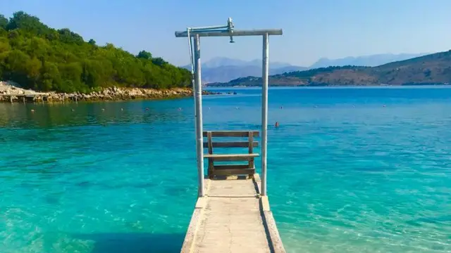 Mały pomost na plaży w Albanii. Woda ma intensywnie błękitny kolor.