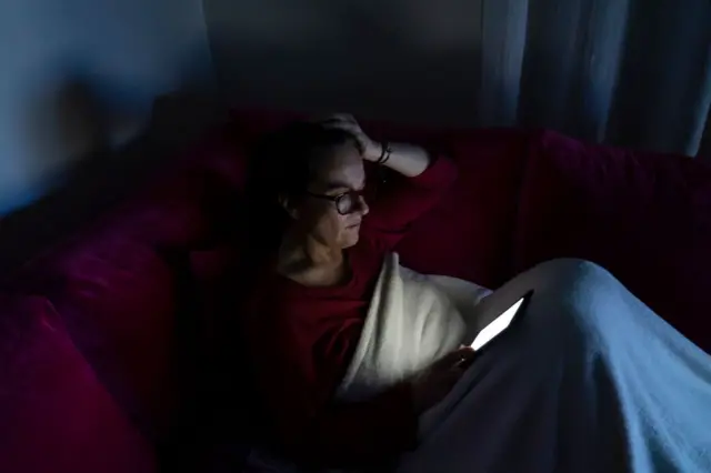 
Uma mulher sentada no sofá lendo algo no tablet. 