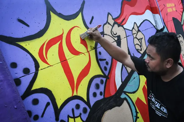 Seorang warga menyelesaikan pembuatan lukisan mural di Kampung Kadu, Curug, Kabupaten Tangerang, Banten, Jumat (16/8/2024).