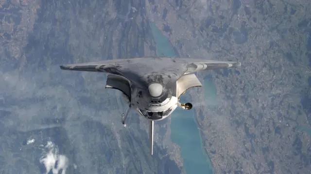 Eileen Collins uzay mekiğini baş aşağı çevirerek komuta ediyor. Uzay mekiğinin arkasında yeryüzü görülüyor.