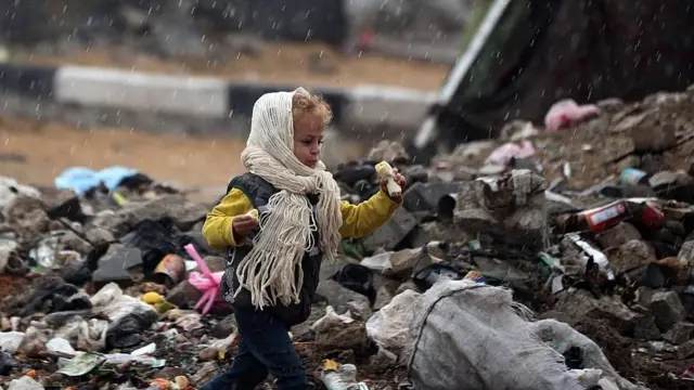 Un niño con bufanda y gorro corre entre un vertedero de desechos