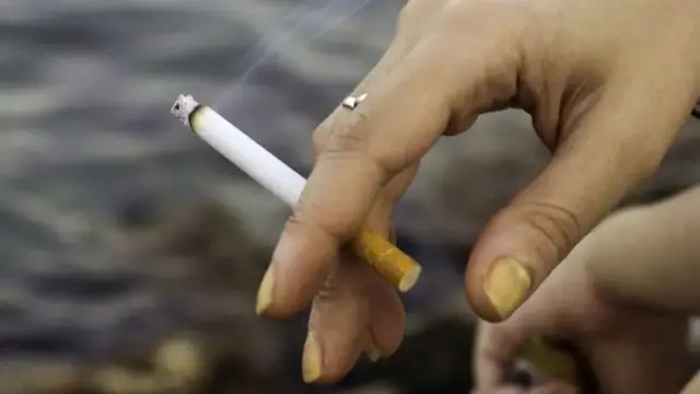 Foto de uma mo com unhas amareladas segurando um cigarro. 