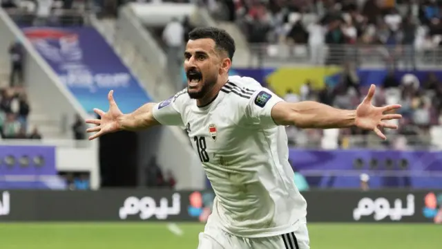 لاعب كرة قدم يحتفل فاتحاً بيديه بتسجيل هدف - قميص أبيض رسمي للمنتخب العراقي - المهاجم أيمن حسين