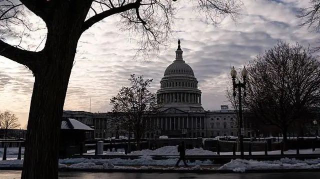 議事堂の手前に雪が積もり、人が歩いている。空は曇っている