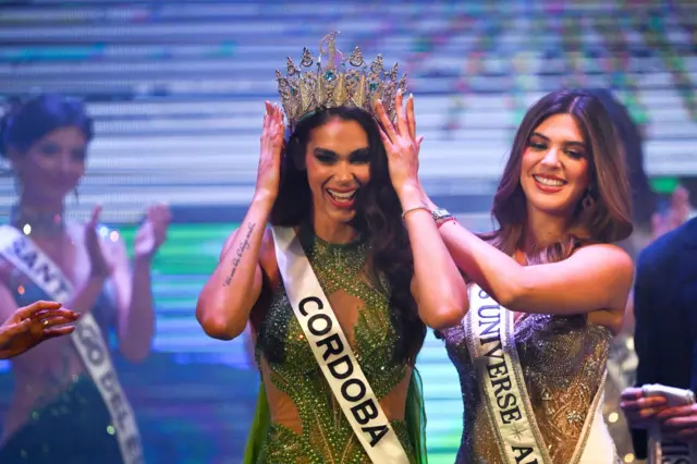 Magaly Benejam, on the left, from Córdoba, raises both hands to touch the crown on her head.