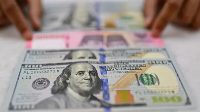 Karyawan memperlihatkan uang pecahan rupiah dan dolar Amerika Serikat (AS) di gerai penukaran mata uang asing Ayu Masagung, Jakarta, Selasa (12/5/2026).