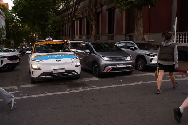 Una persona cruza frente a un taxi y un auto eléctricos en el centro de Montevideo.