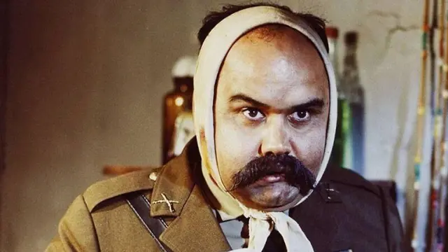 تصویر چهره اکبر عبدی، بازیگر که سر او باندپیچی شده. نمایی است از فیلم «ای ایران»