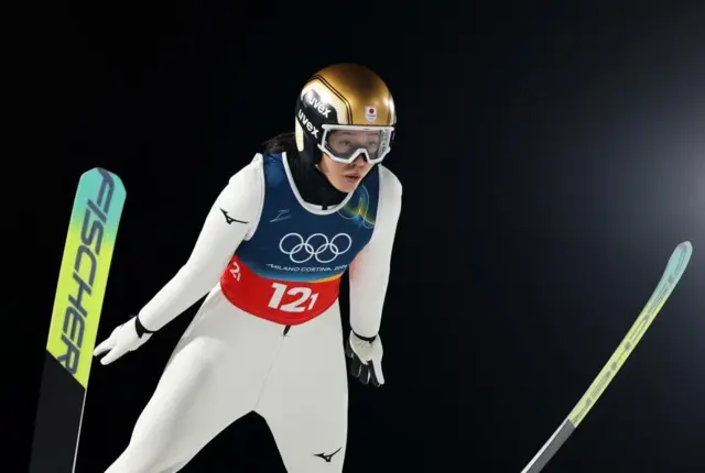 白いウェアの丸山がスキーを開いて飛び前方を見ている