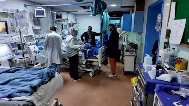 غرفة يظهر فيها أسرّة ومرضى وبعض أقاربهم وطبيب يقوم بعمله.