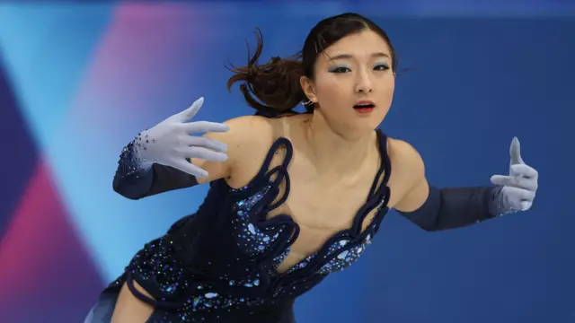 深い青のワンピース型の衣装に、腕から指先にかけて深い青から薄い青のグラデーションになっている手袋を着けた坂本が、両手を広げて演技している
