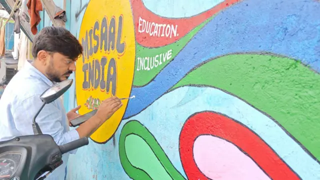 Un hombre pinta un mural en una pared en una comunidad marginal de la ciudad de Bombay.