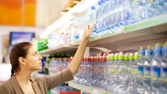 Mulher retira uma garrafa plástica de água mineral da gôndola de um supermercado