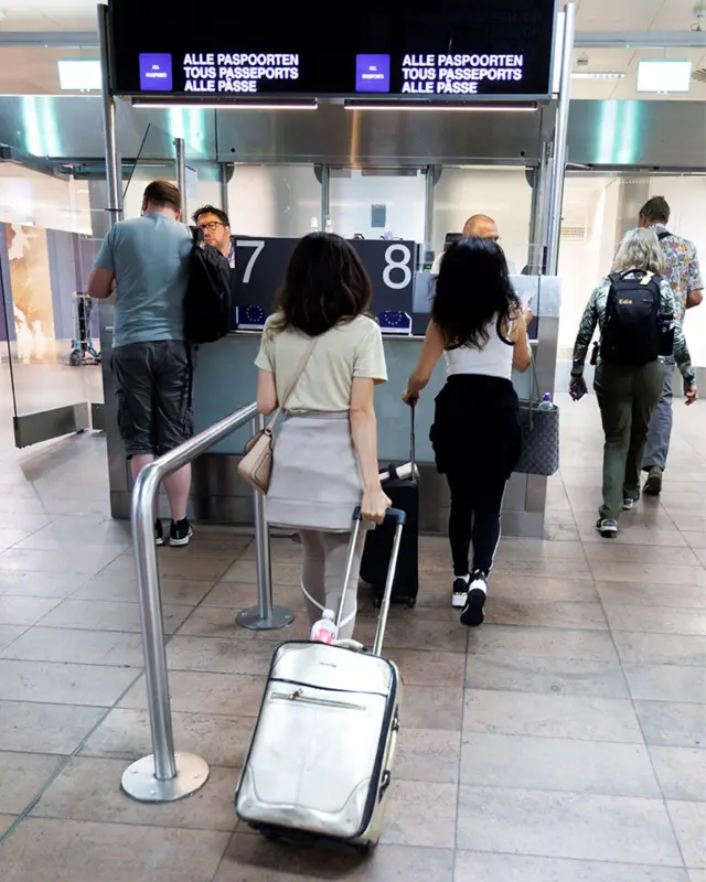 Pasoška kontrola na aerodromu i nekoliko putnika sa koferima 