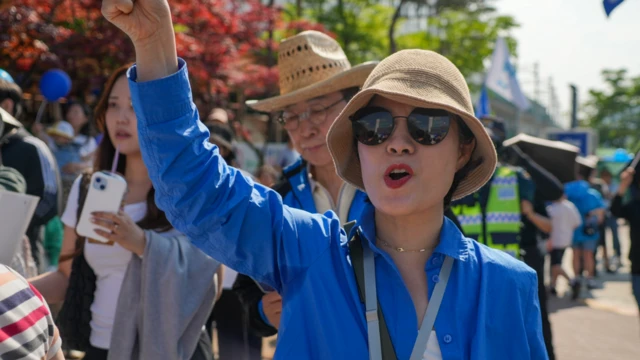 Park Suh-jung stands in a blue jacket at a political rally, waving her hand