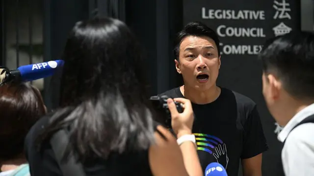 黒いTシャツを着た香港のLGBTQ活動家ジミー・シャム氏が、立法会の外で記者団に応じている