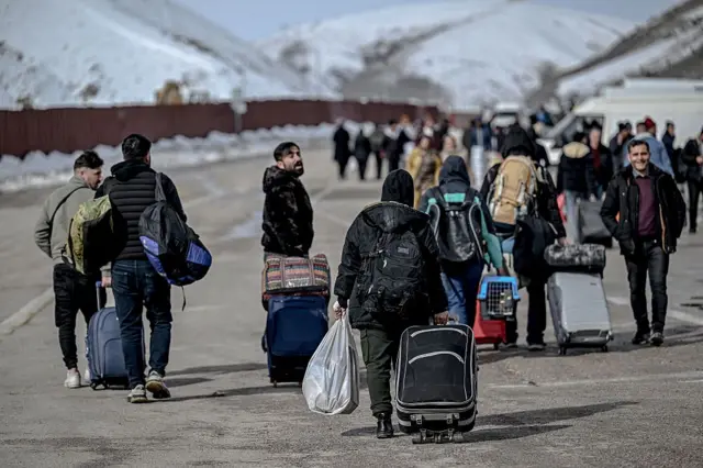 Türkiye'nin kuzeydoğusundaki Razi-Kapıköy sınır kapısından çıkan kalabalık bir grubun, ellerindeki bavullarla minibüslere doğru yürüdüğü görülüyor. 