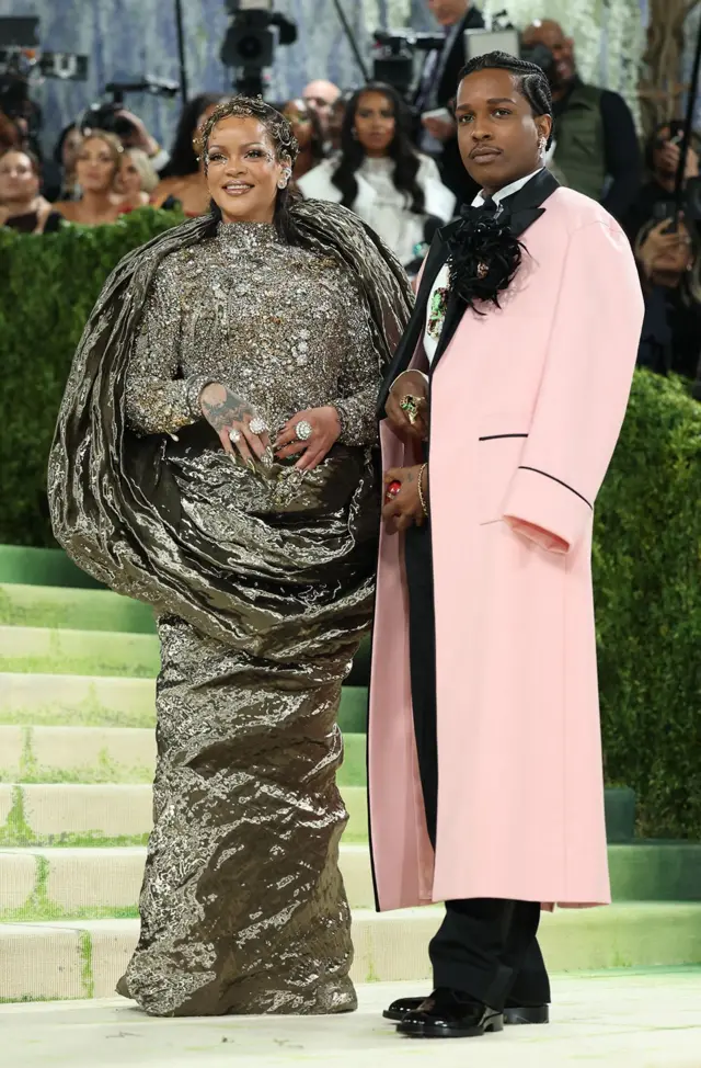 Rihanna ma na sobie srebrną suknię oplatającą sylwetkę, a A$AP Rocky — długi płaszcz w jasnoróżowym kolorze.