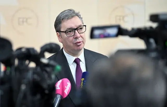 Vucic pembe bir mikrofona konuşuyor, önünde kameranın monitörü görünüyor. 