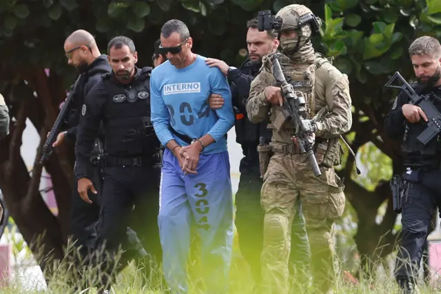 Marcola caminha de algemas e óculos escuros acompanhados por cinco agentes fortemente armados