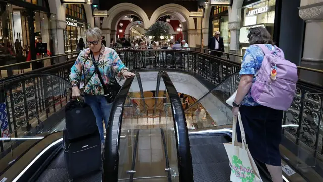 Dos señoras usando la escalera automática de un centro comercial.