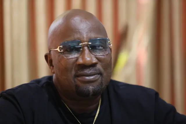 Baba Londoner - o wọ aṣọ dudu pẹlu igo loju rẹ ati ẹgba ọrun