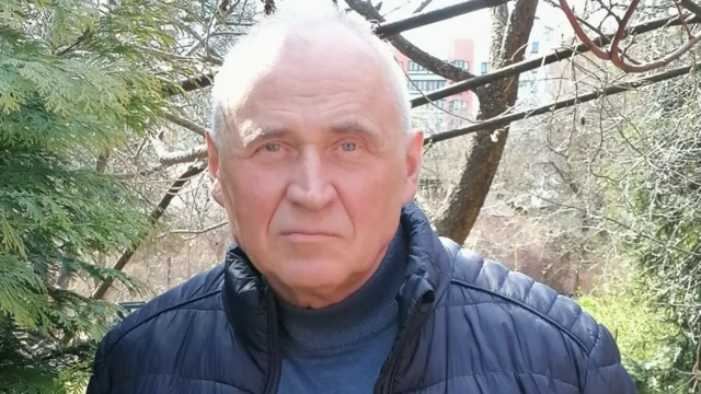 Николай Статкевич , пожилой седой мужчина в синей куртке, на фоне деревьев и виднеющегося вдали многоэтажного дома