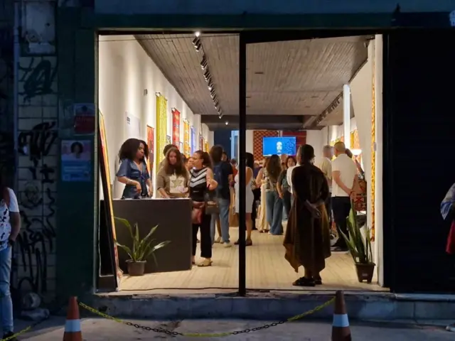 Imagem da entrada de um espaço com uma porta de vidro por onde se vê várias pessoas